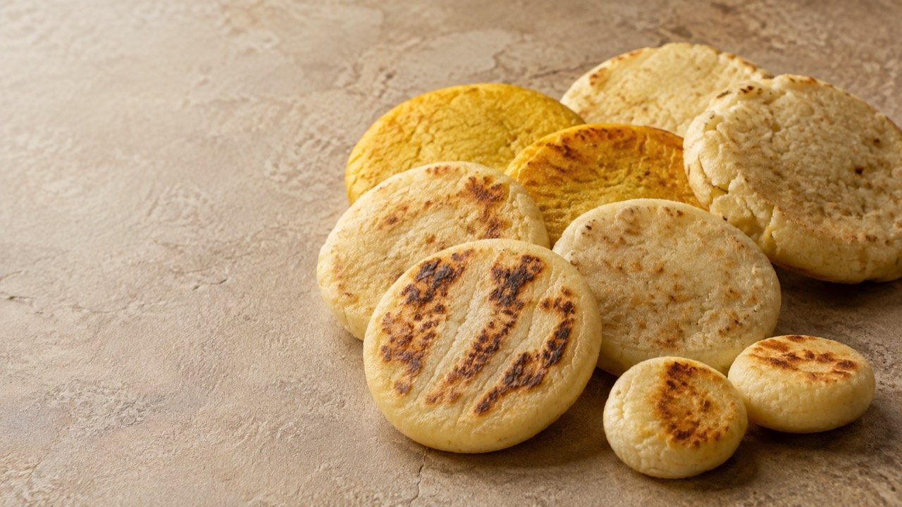 Arepas blancas y amarillas doradas sobre una superficie de piedra.